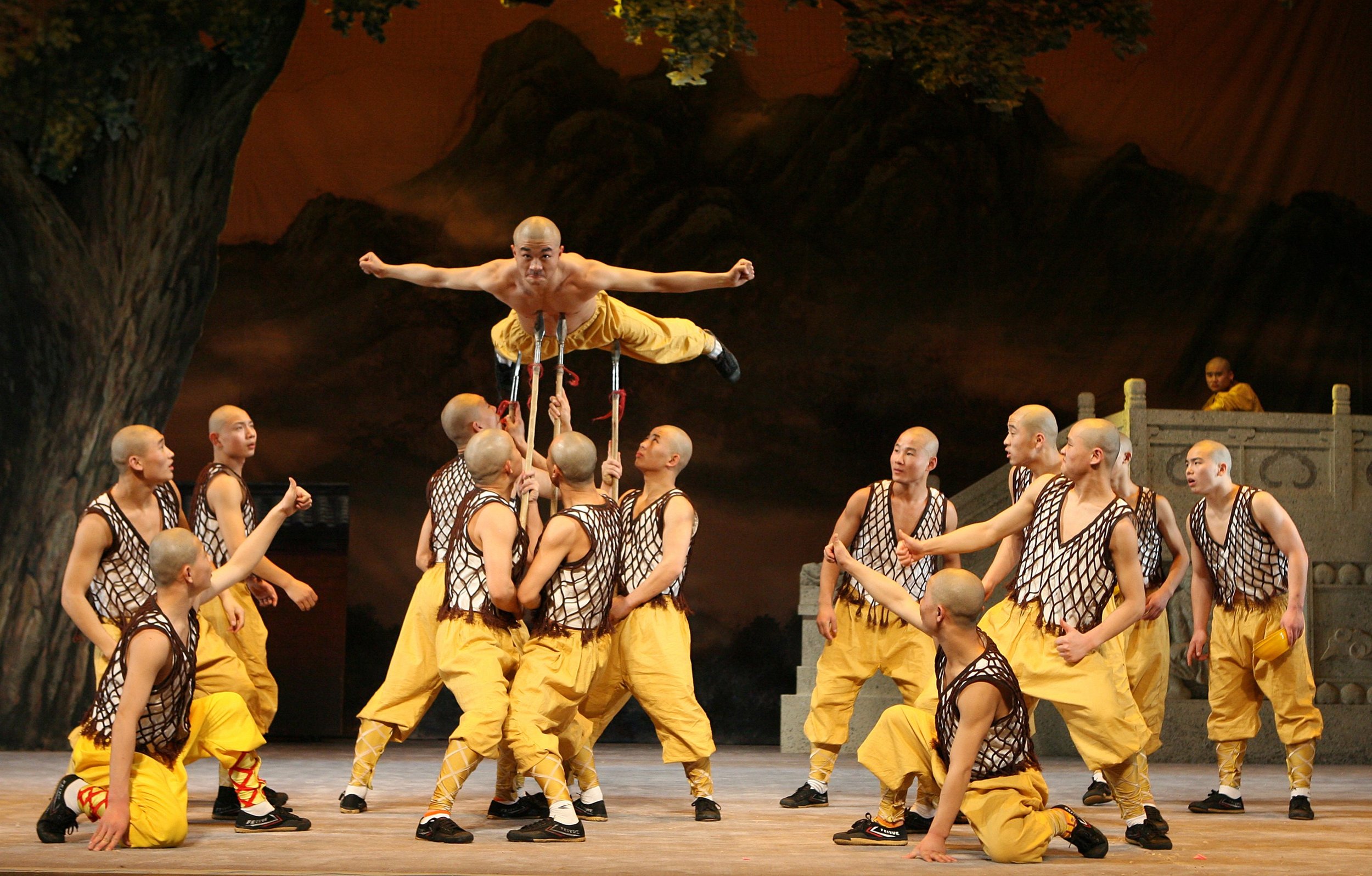 A performer balances above a circle of spear-bearing artists
